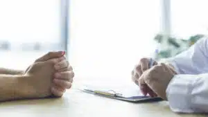 foto ravvicinata delle mani di un paziente e delle mani del medico a tavolino che valutano la situazione