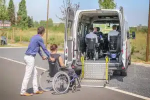 operatore che fa salire una ragazza disabile con carrozzina sul pulmino per disabili con rampa 