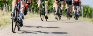 Gruppo di ciclisti in gara su strada asfaltata, circondati da vigneti