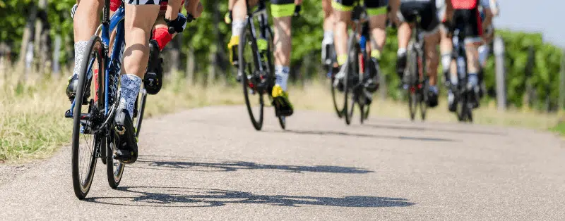 Gruppo di ciclisti in gara su strada asfaltata, circondati da vigneti