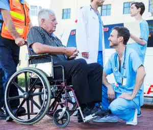 operatori sanitari che portano un paziente disabile sulla carrozzina verso l'ambulanza