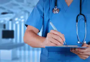 immagine ravvicinata di un medico con camice blu che scrive su una cartellina 