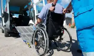 un operatore aiuta una persona anziana su carrozzina a salire su un mezzo sanitario con rampa